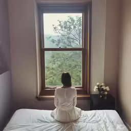 a woman in white sits on the edge of a bed