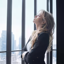 the young woman stands by a window looking out