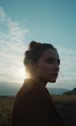 a woman looking down while standing in an open field