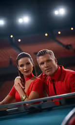 a man and woman are posing with a pool table in front of an empty stadium
