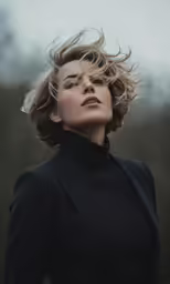 a beautiful blond haired woman with a blazer jacket and long lashes, is photographed in a black dress