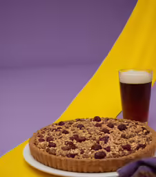 a dessert next to a glass of beer on a purple and yellow tablecloth