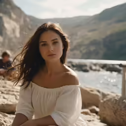 a woman sits on a rock by the water