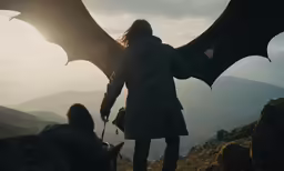 man in long coat standing on a hill with dragon wings spread