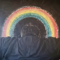 the man is looking at the rainbow and reflection of it