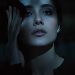 a woman with her hand in her face, standing in the dark