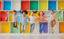 three girls and one boy leaping on a shelf with colorful bookshelves