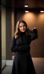 the woman poses in front of a door wearing a long coat and gloves