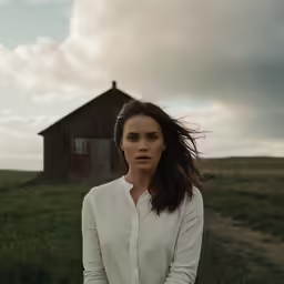a young lady is standing in front of an old barn