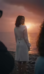 a woman in white dress standing on rocks near the ocean