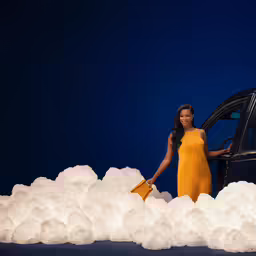 a woman in a yellow dress standing next to a car with white foam balls