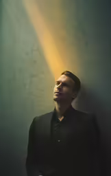 a man stands with his head propped against a wall