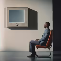 a man sitting in an orange chair next to a square light switch