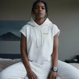a woman sits on a bed with her hands clasped