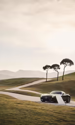 a black car driving on a winding road next to a few trees