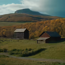 two wooden barns in an open field with mountains in the background