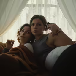 two young women laying next to each other, one with an earbud on and one with a cell phone