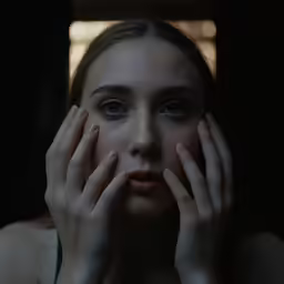 a woman is holding her hands near her face and looking into the camera