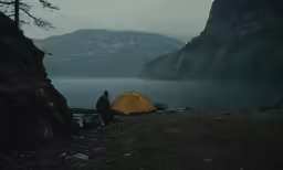 a man standing by a tent on a hill next to the water