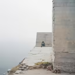 a man sitting next to an ocean near concrete steps