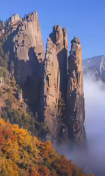 a large rock formation with yellow leaves in the foreground