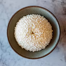 an overhead view of a white rice ball in a green bowl on a marble surface