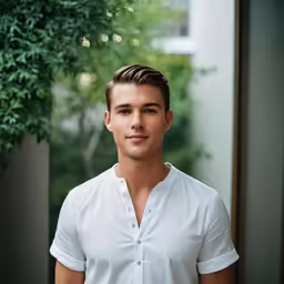 a man in white shirt standing near a tree