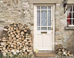 stacked wood in front of an exterior white door with window,a house front entrance with stacked logs sitting on the doorstep