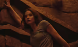 a woman in grey shirt and jeans with her arms up by the rocks
