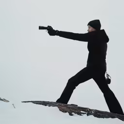 a person holding a camera while standing on a rock