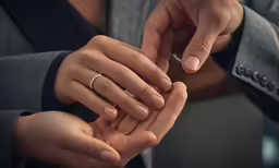 a person is holding a wedding ring and putting it on another persons hand