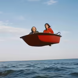 a red boat with two men inside as it floats over a body of water