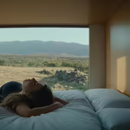 a woman is laying on her bed with mountains in the distance