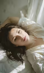 a young woman laying on top of a bed in a white gown