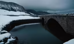 snow covered mountains and a stone bridge in the foreground