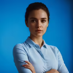 a woman in a blue shirt looking at the camera with her arms crossed