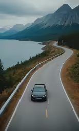 a black car is driving down a highway beside mountains