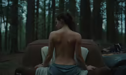 a naked woman standing in the woods near a car