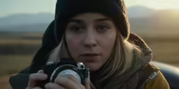 a woman holding a camera while looking at the camera