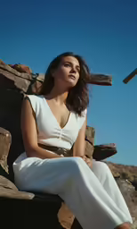 a woman in white sitting on top of a rock wall