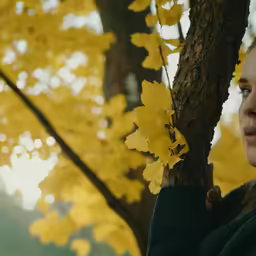 a woman in black standing next to a tree with yellow leaves