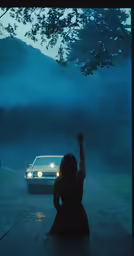 a woman sits on the ground with her arms up as a car drives by at night
