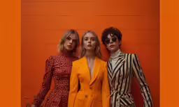 three women in jackets standing in front of a wall
