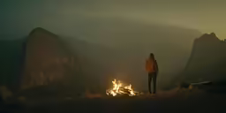 man standing in front of a fire in the mountains