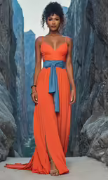 a woman is standing in an orange dress and wearing a necklace
