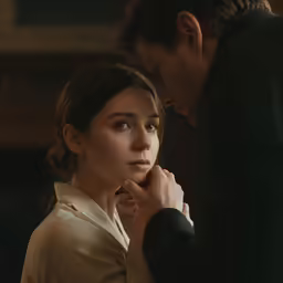 a woman looking at a man who has his hand near her ear