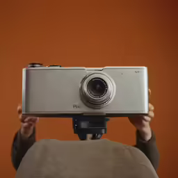 a person holding up a silver camera while taking a photo