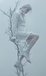 a woman in a white dress sitting on a tree branch