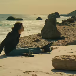 a young lady sitting on a rocky beach near the water