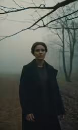 a woman standing in front of trees in a fog